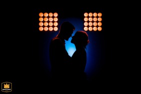 A romantic wedding photo capturing a couple about to kiss at their celebration in Salle polyvalente, Tossiat, France. The bride and groom are beautifully silhouetted against a blue gel light backdrop, creating a dreamy and intimate atmosphere.